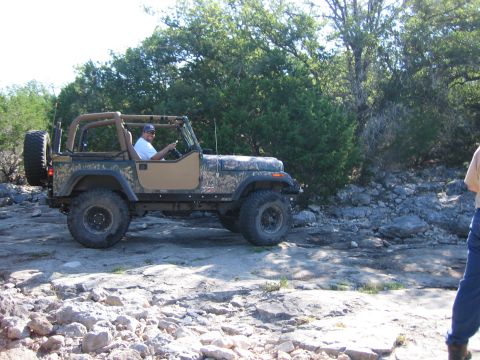 1996 Ford Bronco - A camouflaged Jeep Wrangler navigates a rocky trail with a driver behind the wheel.