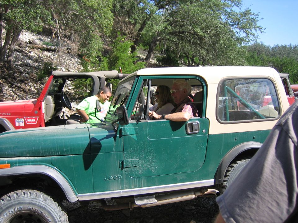 Green and tan Jeep CJ-7 with people inside, parked next to a red Jeep