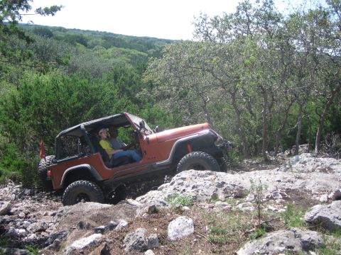 1996 Ford Bronco - A Jeep Wrangler drives over rocks and brush on an off-road trail.