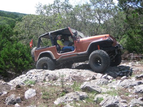 1996 Ford Bronco - An orange Jeep Wrangler navigates a rocky trail with two occupants visible.