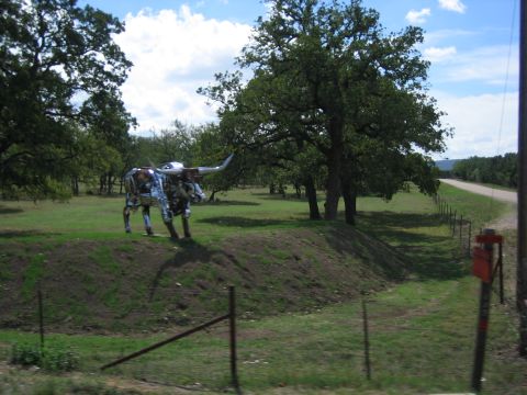 1996 Ford Bronco - Metal longhorn sculpture stands in a field with trees and a dirt road nearby.