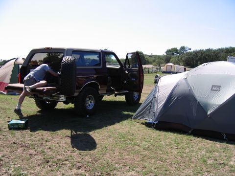 1996 Ford Bronco - A person loads gear into a maroon Ford Bronco parked at a campsite next to tents.