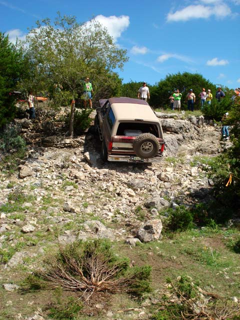 1996 Ford Bronco - A two-tone Ford Bronco navigates a steep, rocky terrain with spectators watching.