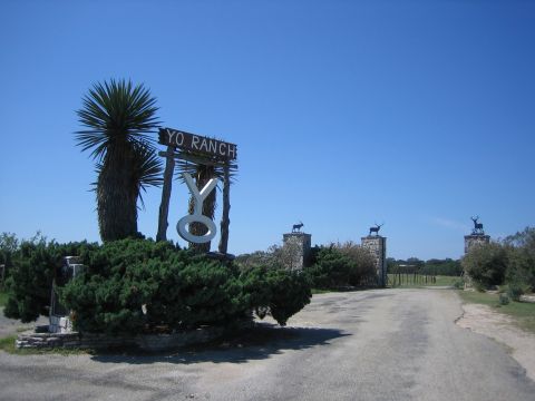 1996 Ford Bronco - The entrance to Yo Ranch features a prominent sign, lush greenery, and decorative stone pillars topped with animal figures.
