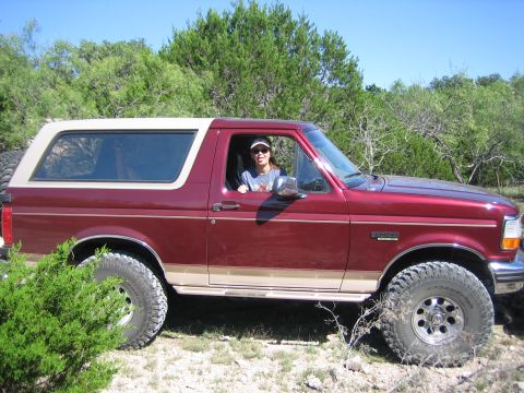 1996 Ford Bronco - A maroon and tan Ford Bronco with a removable top is parked outdoors.