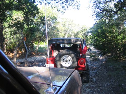 1996 Ford Bronco - A convoy of Jeeps navigates a rough, off-road path surrounded by trees.