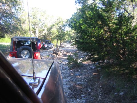 1996 Ford Bronco - Multiple Jeep Wranglers navigate a rocky, wooded trail under a bright sky.