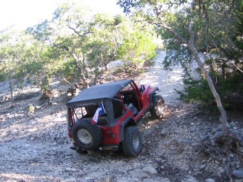 1996 Ford Bronco - Red Jeep Wrangler tackling an off-road trail with a Texas flag on the spare tire.