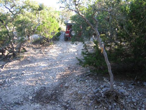1996 Ford Bronco - A red Jeep Wrangler navigates a rough, off-road path surrounded by trees and brush.