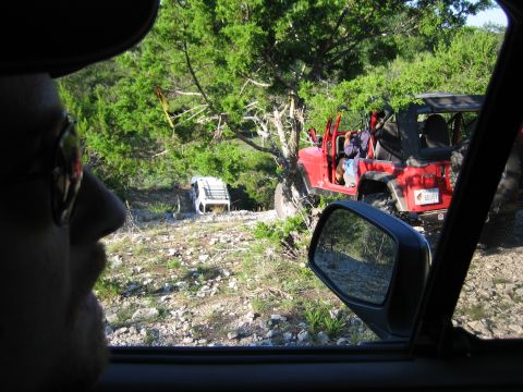 1996 Ford Bronco - Two Jeep Wranglers are seen off-road, one red and one white, navigating a rocky, wooded area.