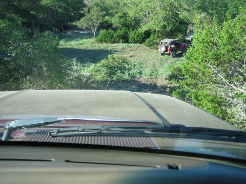 1996 Ford Bronco - Two vehicles are seen off-roading in a natural, wooded environment.