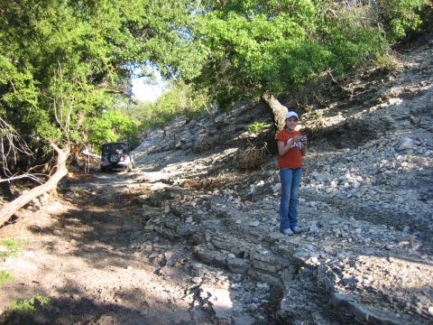 1996 Ford Bronco - A silver Jeep Wrangler navigates a rough dirt road through a wooded area, with a young girl observing from the side.