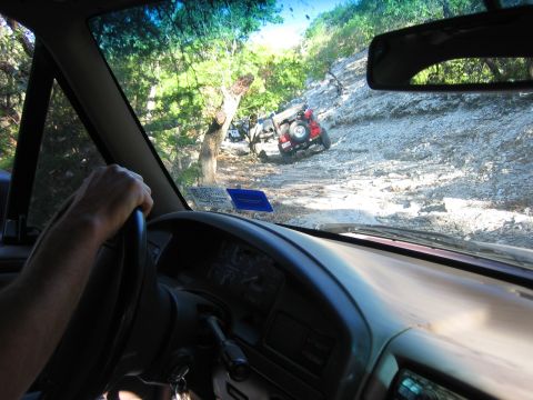 1996 Ford Bronco - Two vehicles navigate a challenging, rocky trail surrounded by trees and brush.