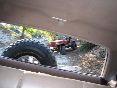 1996 Ford Bronco - An orange Jeep Wrangler drives on a dirt path, viewed from inside another vehicle.