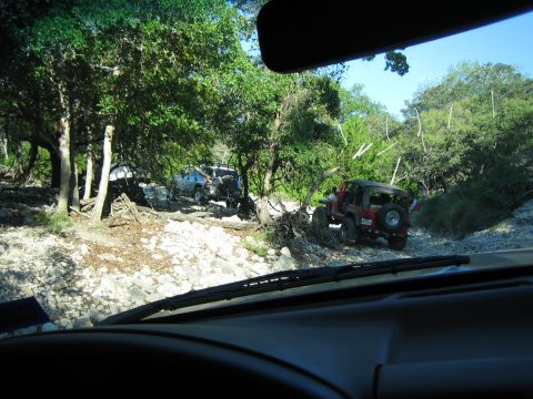 1996 Ford Bronco - Multiple off-road vehicles navigate a challenging rocky terrain surrounded by trees.