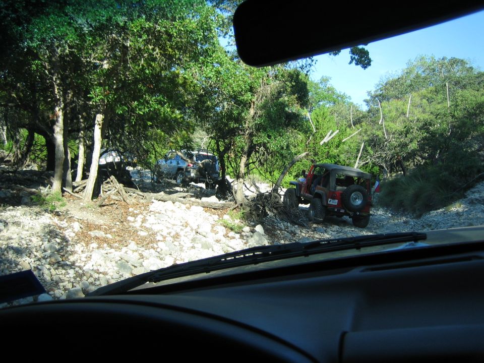 Red Jeep on a rocky trail with other vehicles in the background