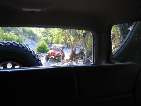 1996 Ford Bronco - Two Jeeps navigate a wooded, rocky trail, suggesting an off-road adventure.
