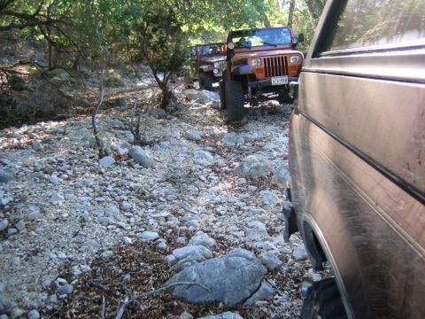 1996 Ford Bronco - Multiple Jeeps navigate a rough, rocky path through a wooded area.