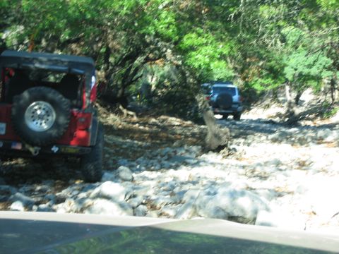 1996 Ford Bronco - Two off-road vehicles navigate a rocky path through a wooded area.