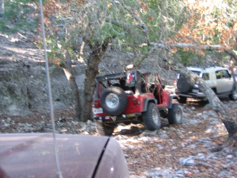 1996 Ford Bronco - A red Jeep Wrangler is seen parked off-road, with a white SUV visible behind it on a rocky trail.