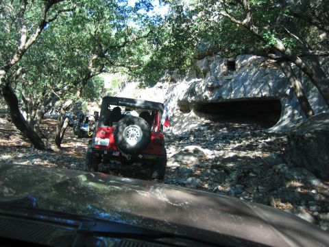 1996 Ford Bronco - Multiple Jeeps navigate a rocky, wooded path near a cave opening.