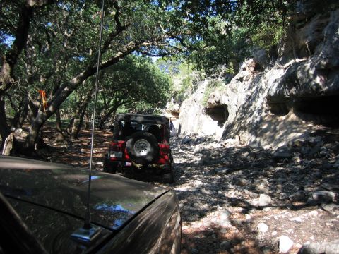 1996 Ford Bronco - Two vehicles navigate a , rocky path through a wooded area with rock formations on the side.