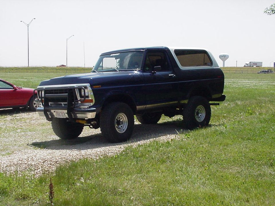 Lifted dark blue 1978-79 Ford Bronco with brush guard on gravel in a field