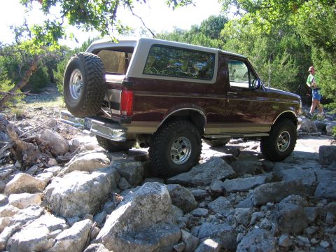 1996 Ford Bronco - A maroon Ford Bronco navigates a rocky trail with trees and foliage in the background.