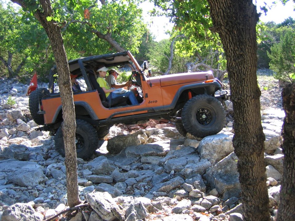Orange Jeep Wrangler navigating a rocky trail, driver and passenger visible