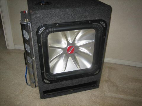 1995 Ford Bronco - A Kicker subwoofer box with a silver cone and black surround is shown, with visible wiring and a chrome heat sink on the side.