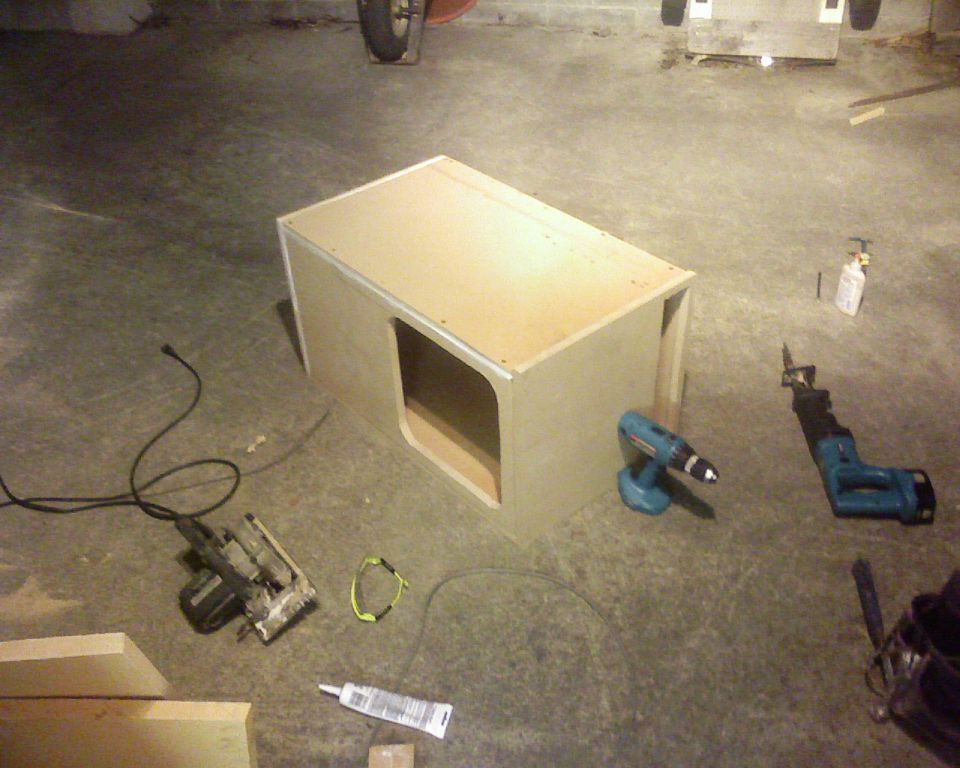 wooden box with cutout, circular saw, drill, and reciprocating saw on concrete floor