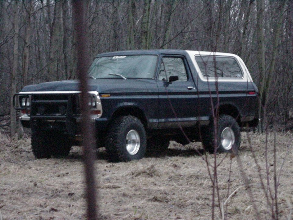 Lifted dark blue Ford Bronco with white top and brush guard parked in a field