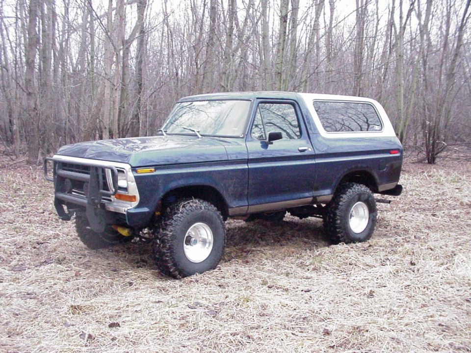 Dark blue Ford Bronco with a white top parked in a wooded area