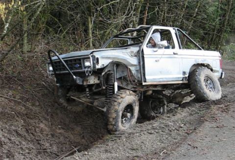 1984 Ford Bronco II - This heavily modified SUV is navigating a muddy trail with its driver visible.