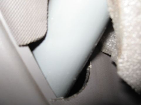 1994 Ford Bronco - Extreme close-up of a light gray plastic interior trim piece or handle emerging through a cut opening in dark upholstery, with tan headline…