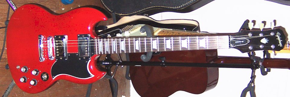 Red Epiphone electric guitar on a stand, with another guitar behind it