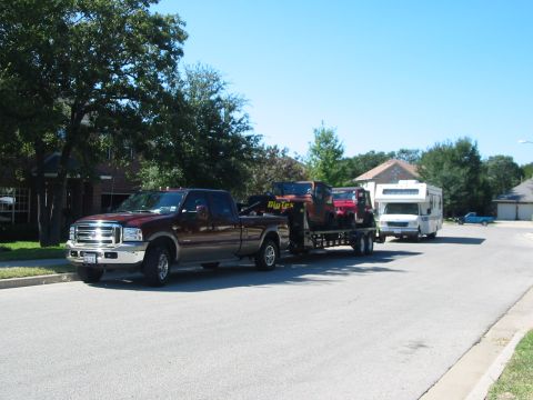 1996 Ford Bronco - A maroon Ford F-250 Super Duty pickup truck tows a trailer carrying two Jeeps and an RV down a suburban street.