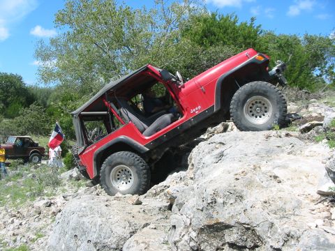 1996 Ford Bronco - A red Jeep Wrangler navigates a rocky trail, with another vehicle visible in the distance.