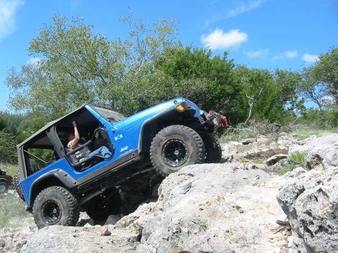 1996 Ford Bronco - A blue Jeep Wrangler navigates a rocky off-road trail under a bright blue sky.