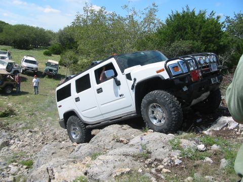 1996 Ford Bronco - A white Hummer H2 is shown off-roading on a rocky slope with other vehicles in the background.