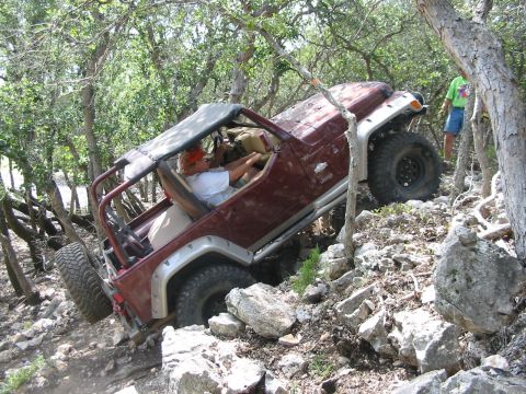 1996 Ford Bronco - A maroon Jeep Wrangler navigates a challenging rocky terrain, with a driver behind the wheel.