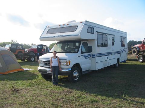 1996 Ford Bronco - A white motorhome with blue racing stripes is parked on a grassy field, accompanied by a tent and several other vehicles.