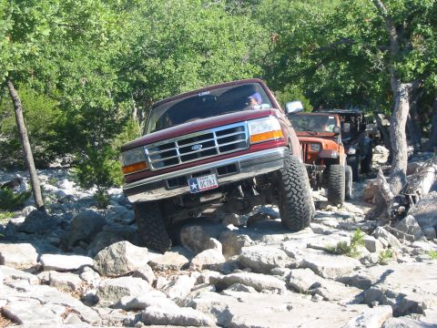 1996 Ford Bronco - This Ford F-Series truck is tackling a challenging off-road trail with other vehicles following.
