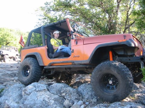 1996 Ford Bronco - An orange Jeep Wrangler navigates a rocky trail with a passenger inside. Another Jeep is seen in the background.