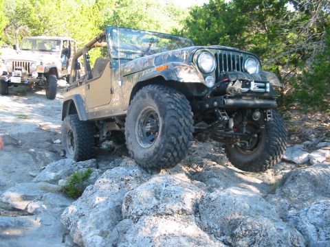 1996 Ford Bronco - Two Jeeps off-roading on a rocky trail with trees in the background.
