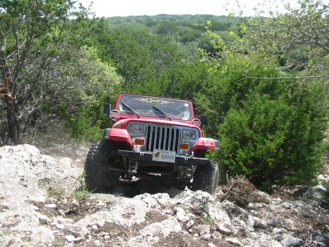 1996 Ford Bronco - A red Jeep Wrangler navigates a challenging rocky terrain on an off-road trail.