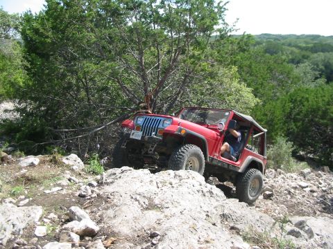 1996 Ford Bronco - A red Jeep Wrangler navigates a challenging rocky trail, demonstrating its off-road capabilities.