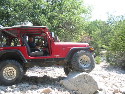 1996 Ford Bronco - A red Jeep Wrangler is shown driving over a large rock on a trail, with a driver behind the wheel.