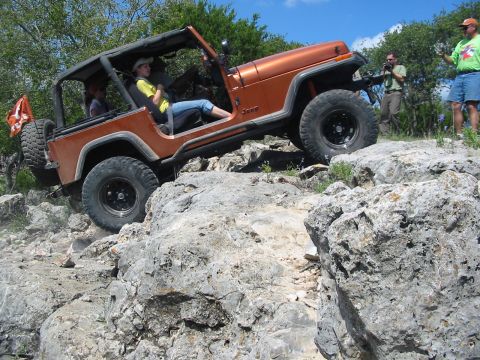 1996 Ford Bronco - A Jeep navigates a rocky trail with spectators observing the off-road adventure.