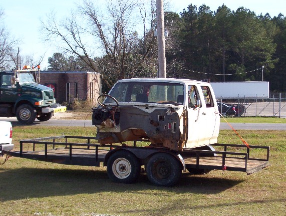 pickup truck cab on a trailer, front of a green truck in background